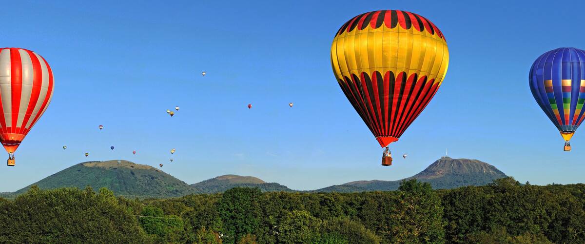 A landscape with a mountain range and hot air balloons in the sky.