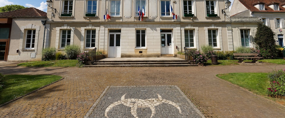 A historic building with a sign reading "HOTEL DE VILLE," flags, and a cobblestone pathway.
