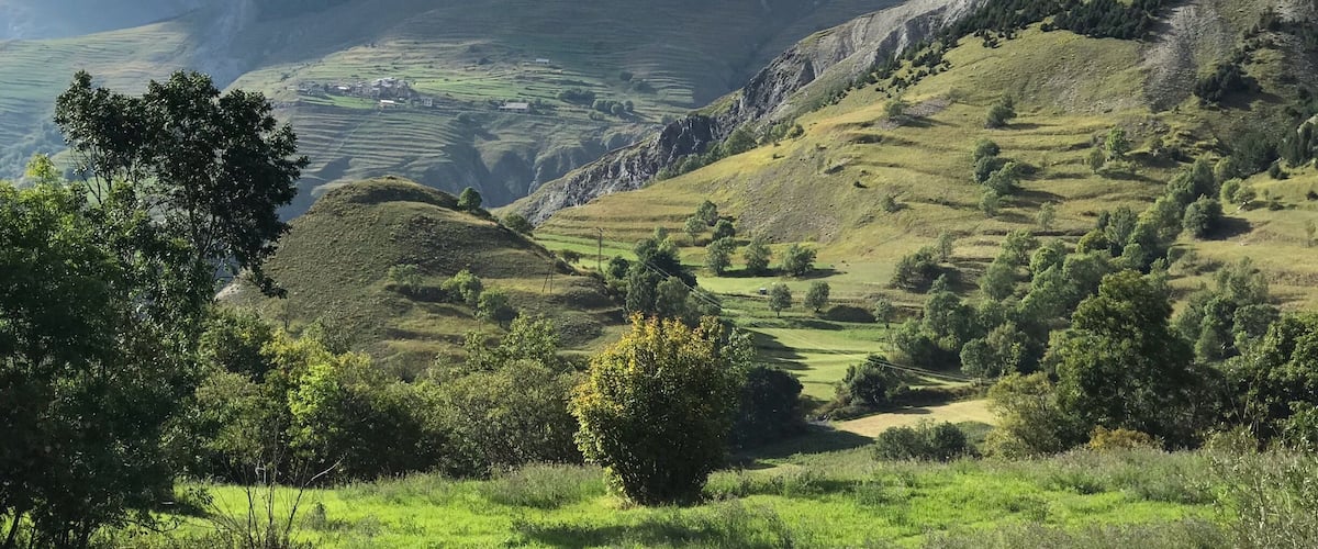 Rolling hills, a valley, and a distant mountain range under a partly cloudy sky.