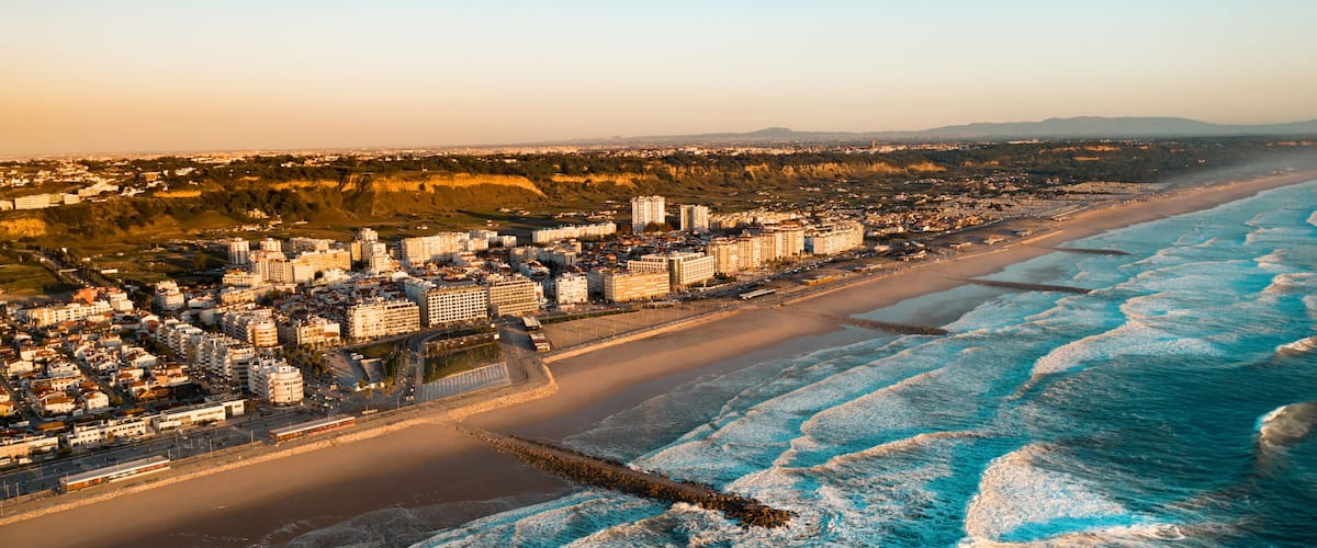 The Aerial footage of Costa da Caparica coastline of glorious sandy beaches, powerful Atlantic waves. City near the ocean.