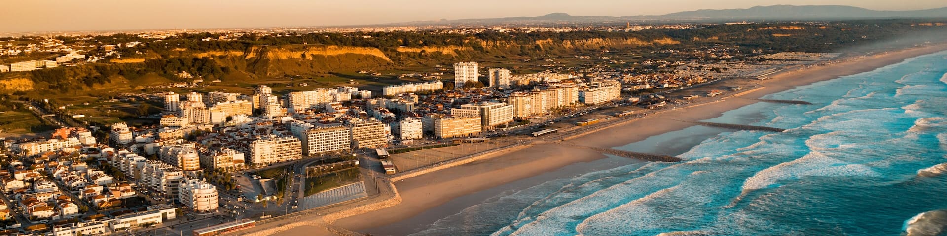 The Aerial footage of Costa da Caparica coastline of glorious sandy beaches, powerful Atlantic waves. City near the ocean.