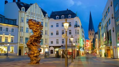 A city square with historic buildings, a tall spire, and a large abstract sculpture.