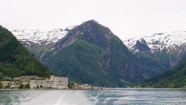 A fjord with a mountain in the background, a small town with buildings along the water's edge, and snow-capped peaks.