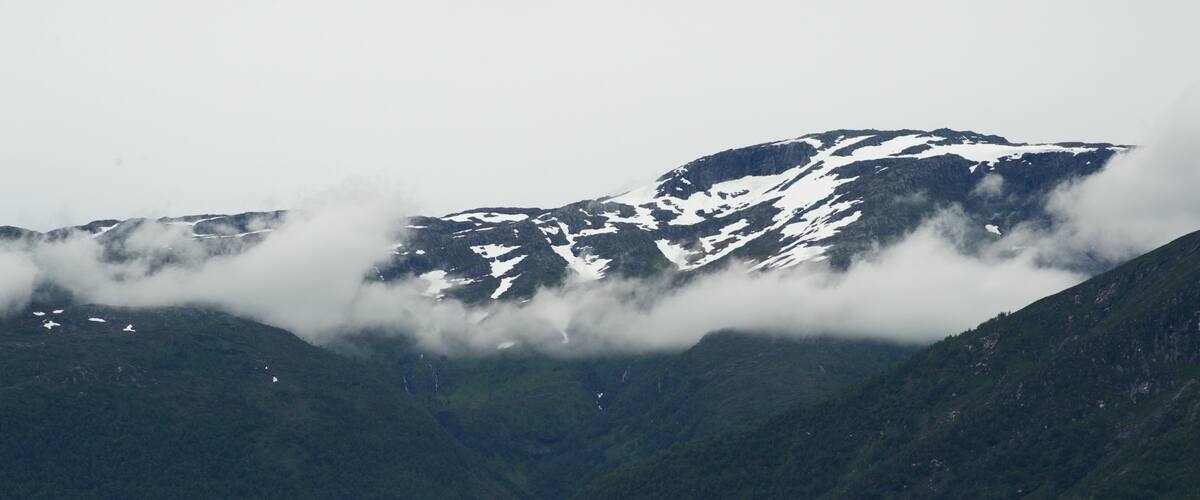 A mountain with snow patches and clouds.