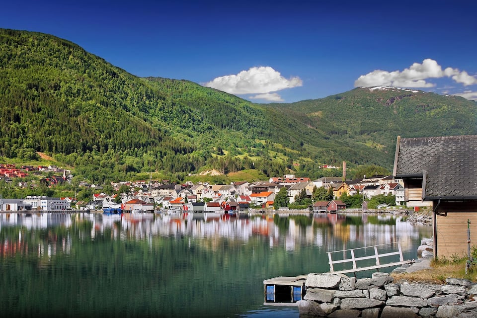 A serene lake with a town and forested hills in the background.