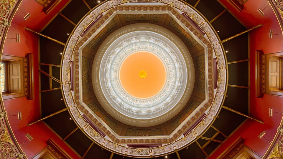 A grand, ornate architectural interior with a central circular design, red walls, and gold detailing.