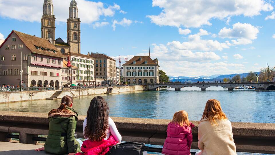 A river with a bridge, historic buildings, and two towers.