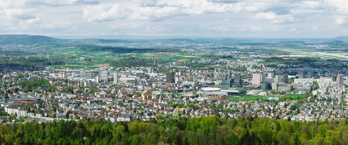 A cityscape with dense urban buildings, a prominent stadium, and a distant airport.