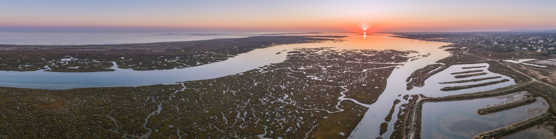 A coastal landscape with a sunset, salt flats, and a distant city.