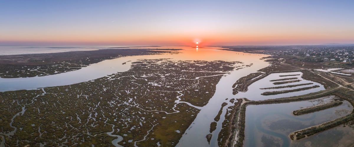 A coastal landscape with a sunset, salt flats, and a distant city.