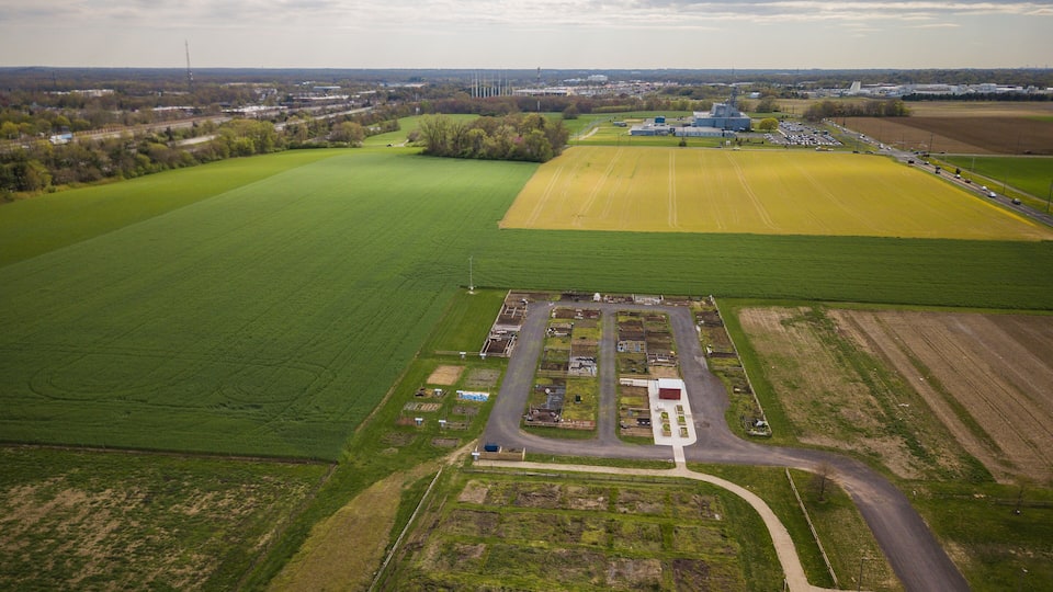 An aerial view of a rural area with green fields, a parking lot, and a large industrial building.