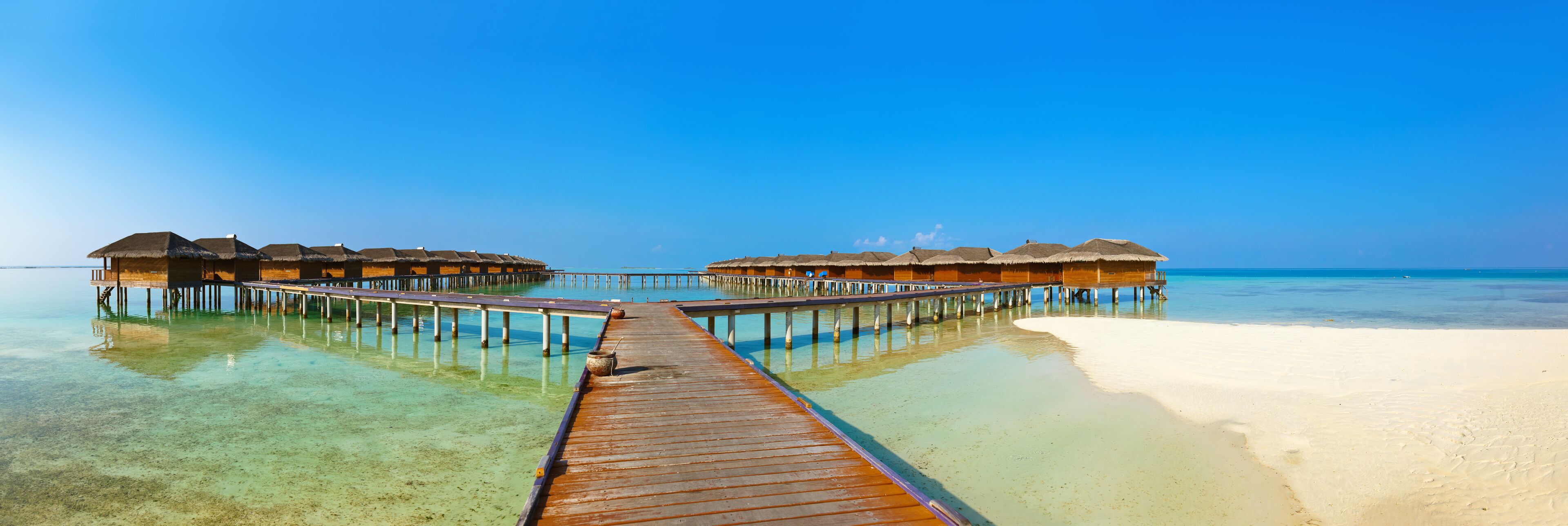 A wooden pier leading to overwater bungalows with thatched roofs.