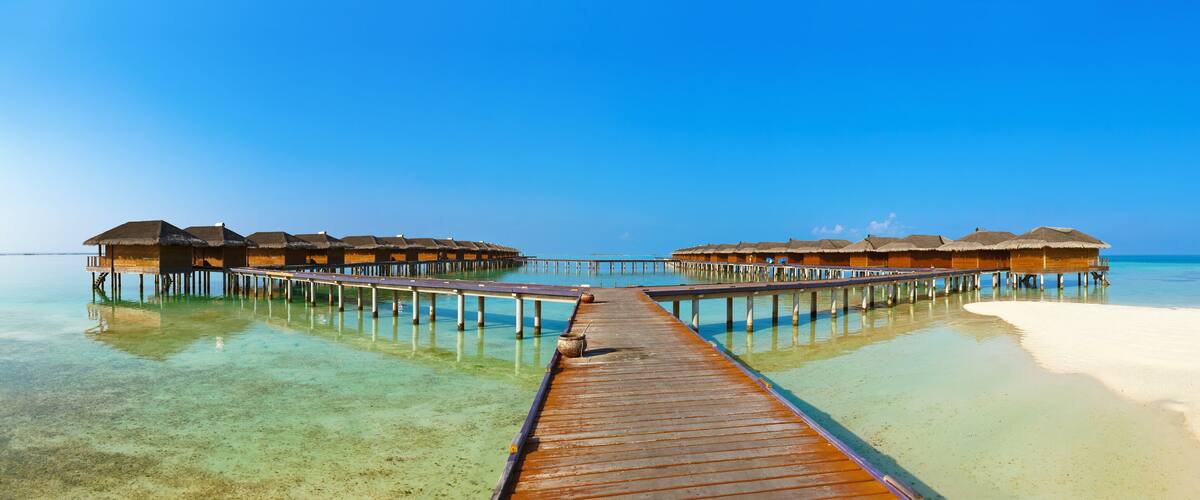 A wooden pier leading to overwater bungalows with thatched roofs.