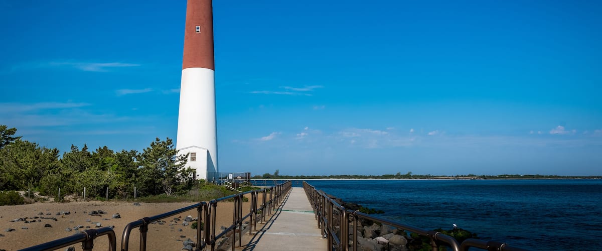 A tall red and white lighthouse with a walkway leading to it, overlooking a calm sea.