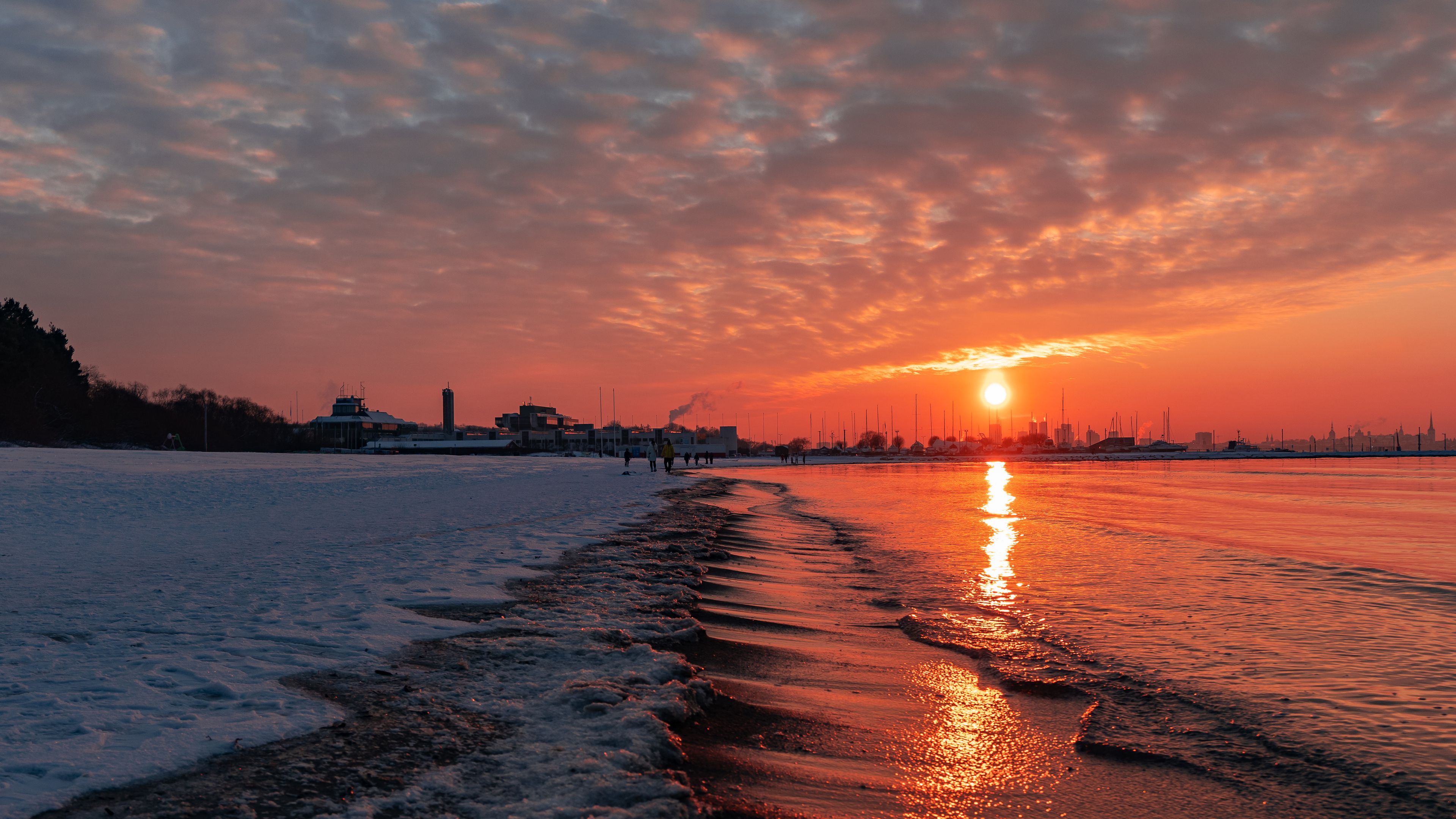 A sunset over a frozen lake with buildings in the background.