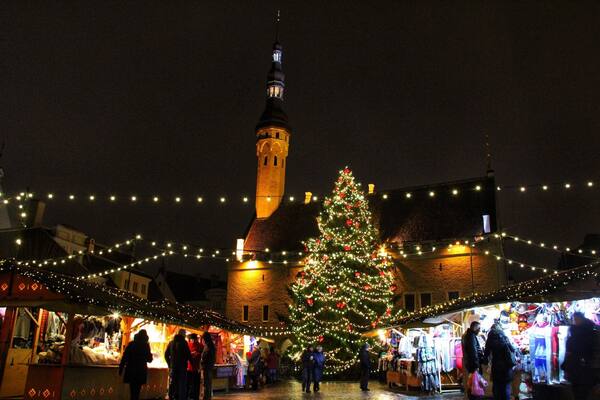 A medieval tower, a decorated Christmas tree, and market stalls at night.