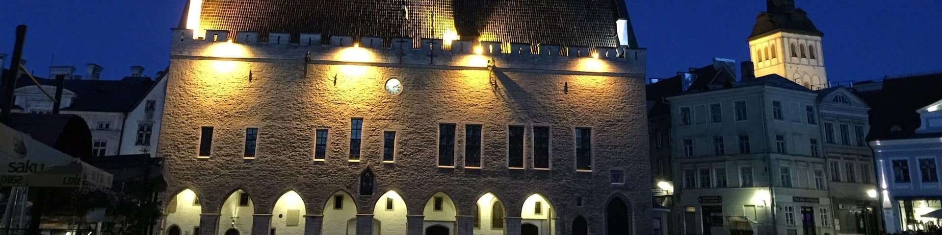 A historic building with a prominent tower and two spires, illuminated at dusk.