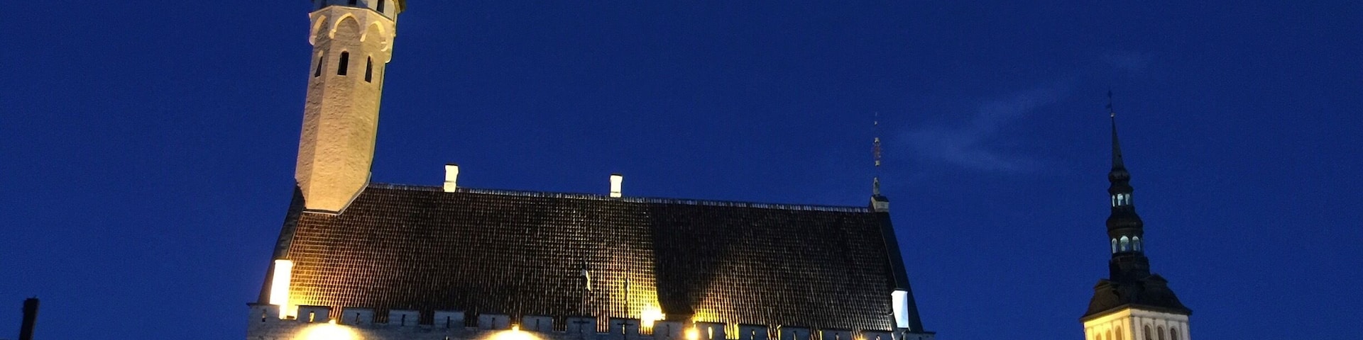 Um edifício histórico com uma torre imponente e duas torres, iluminado ao anoitecer.