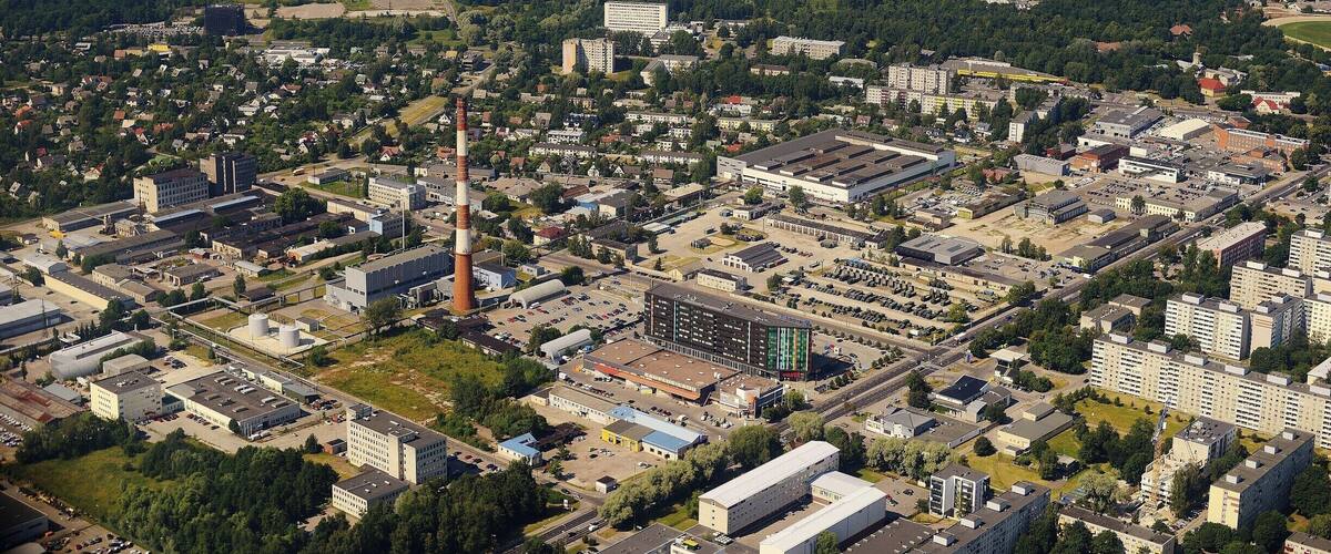 An aerial view of a coastal city with a mix of residential, commercial, and industrial areas, including a prominent factory and a beach in the background.