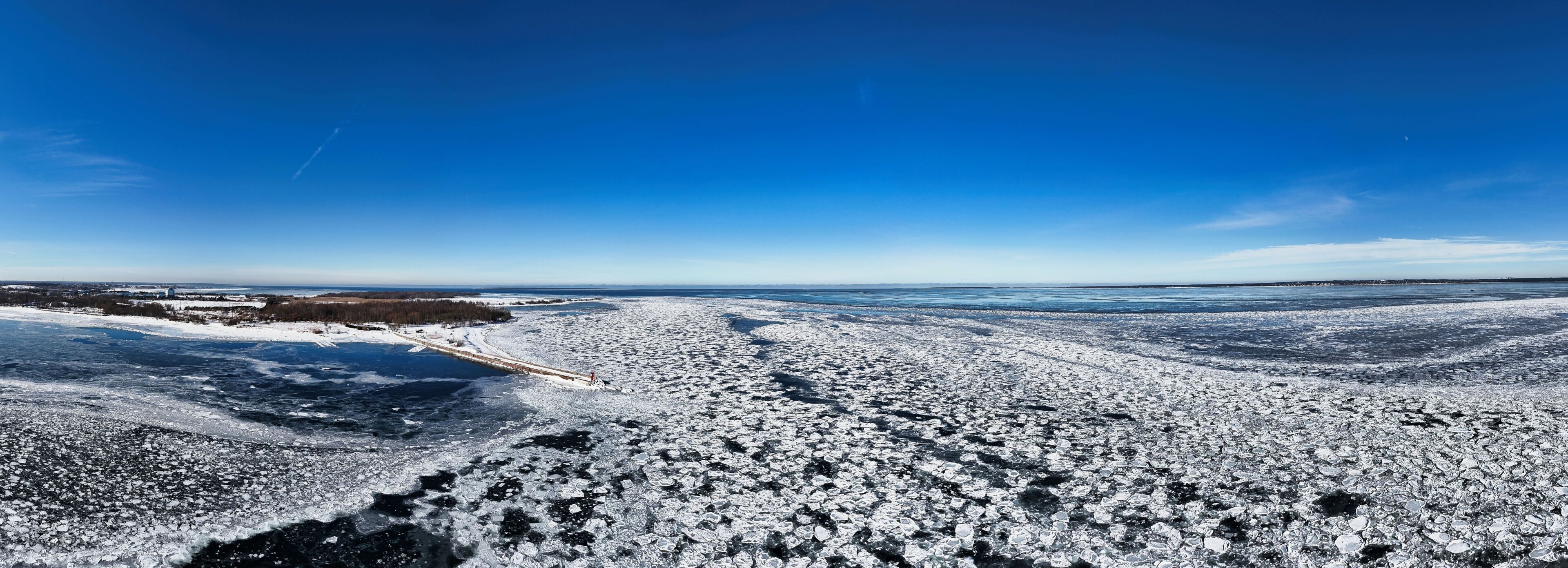 Un paisaje helado con cielo azul despejado, un río congelado y un bosque distante.