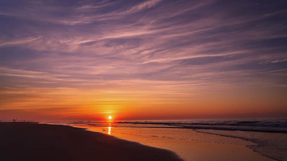 A sunset over a beach with waves and a clear sky.