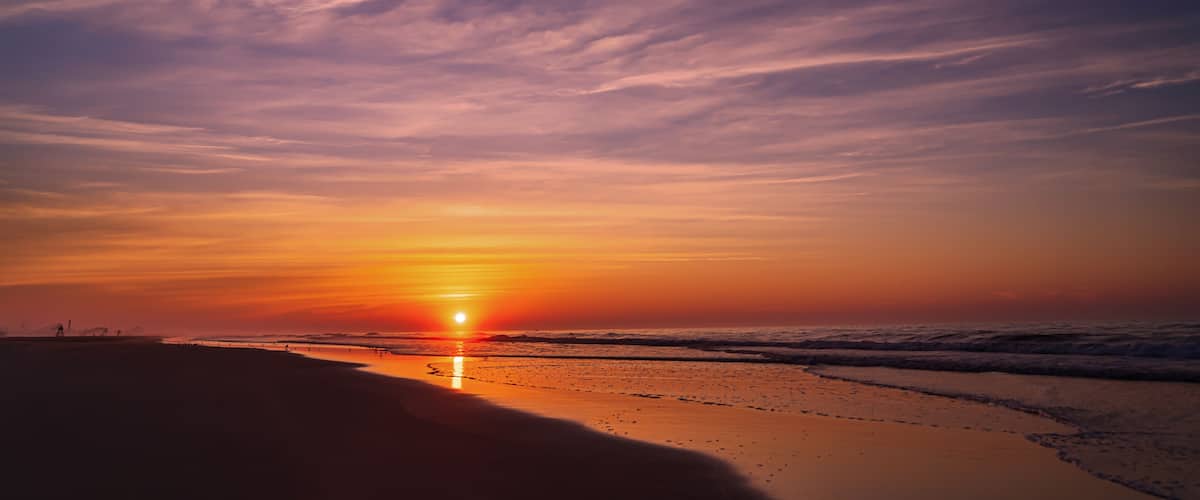A sunset over a beach with waves and a clear sky.