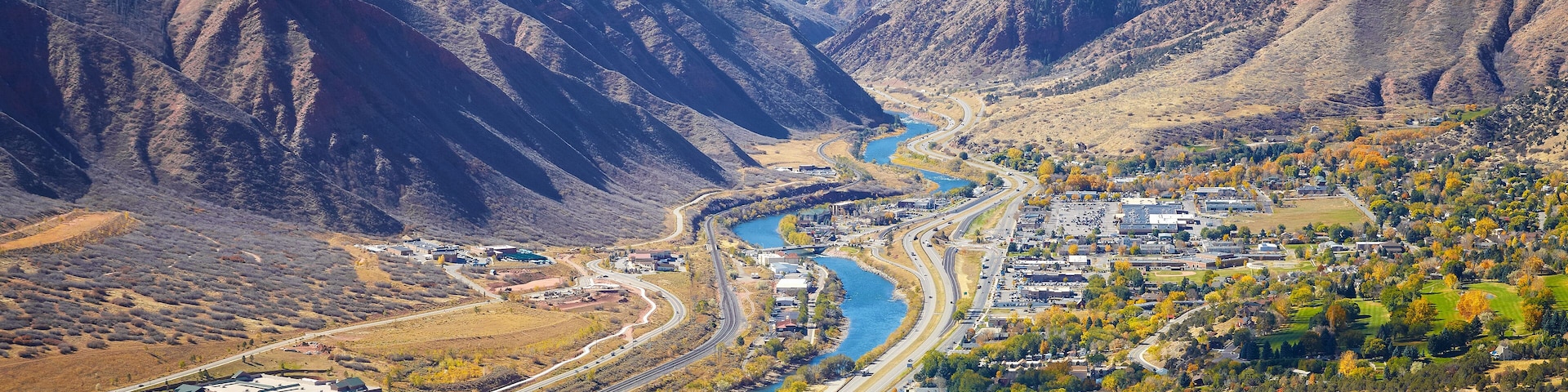 A mountainous landscape with a winding river, a highway, and a town with autumn-colored trees.