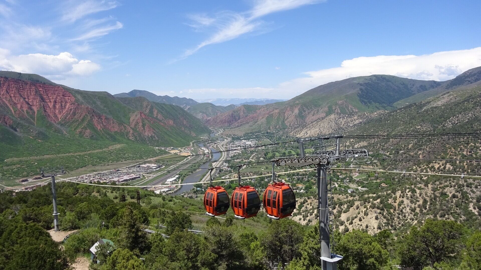 A cable car system in a mountainous area with a river and buildings in the valley below.