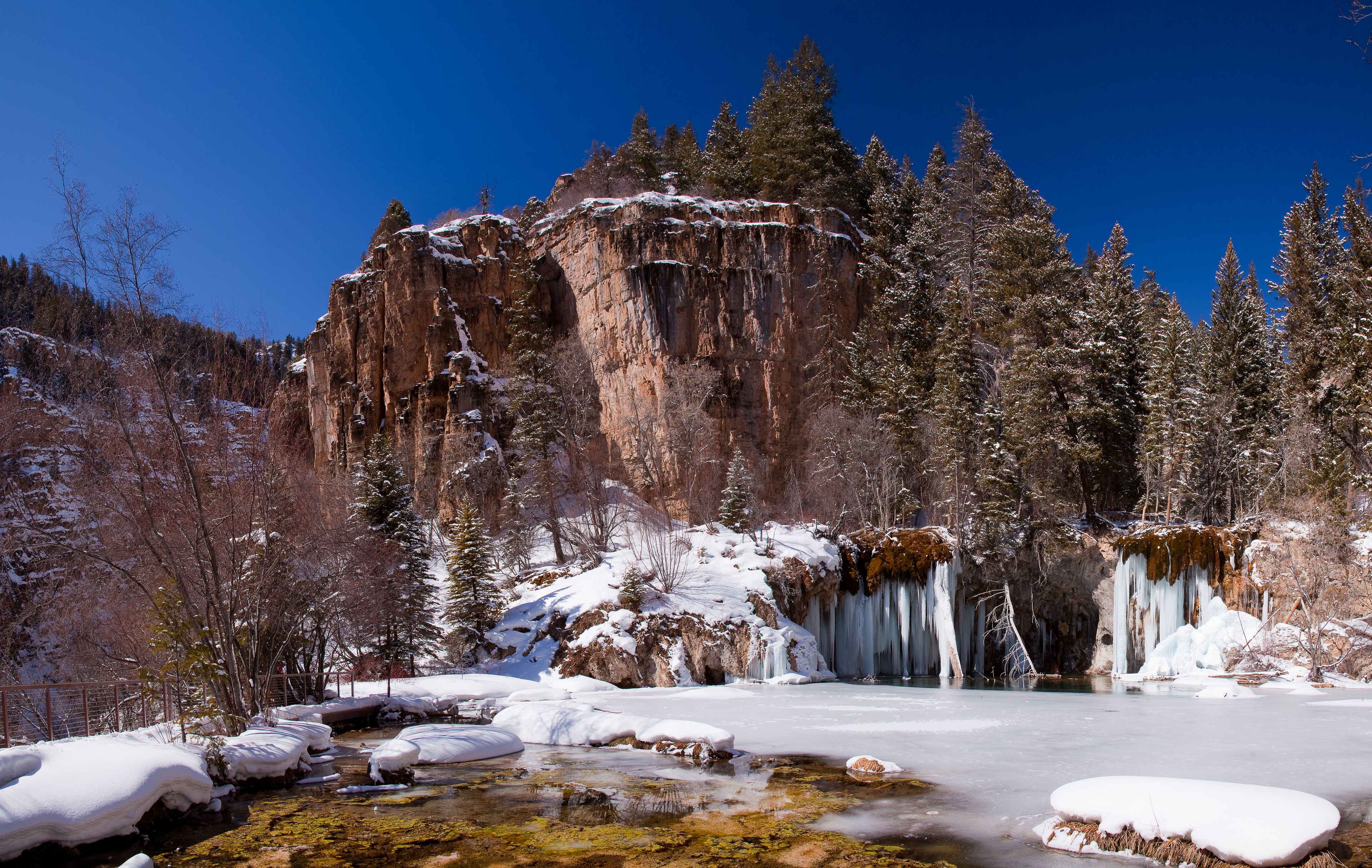 A frozen river with icicles, snow-covered trees, and a rocky cliff.