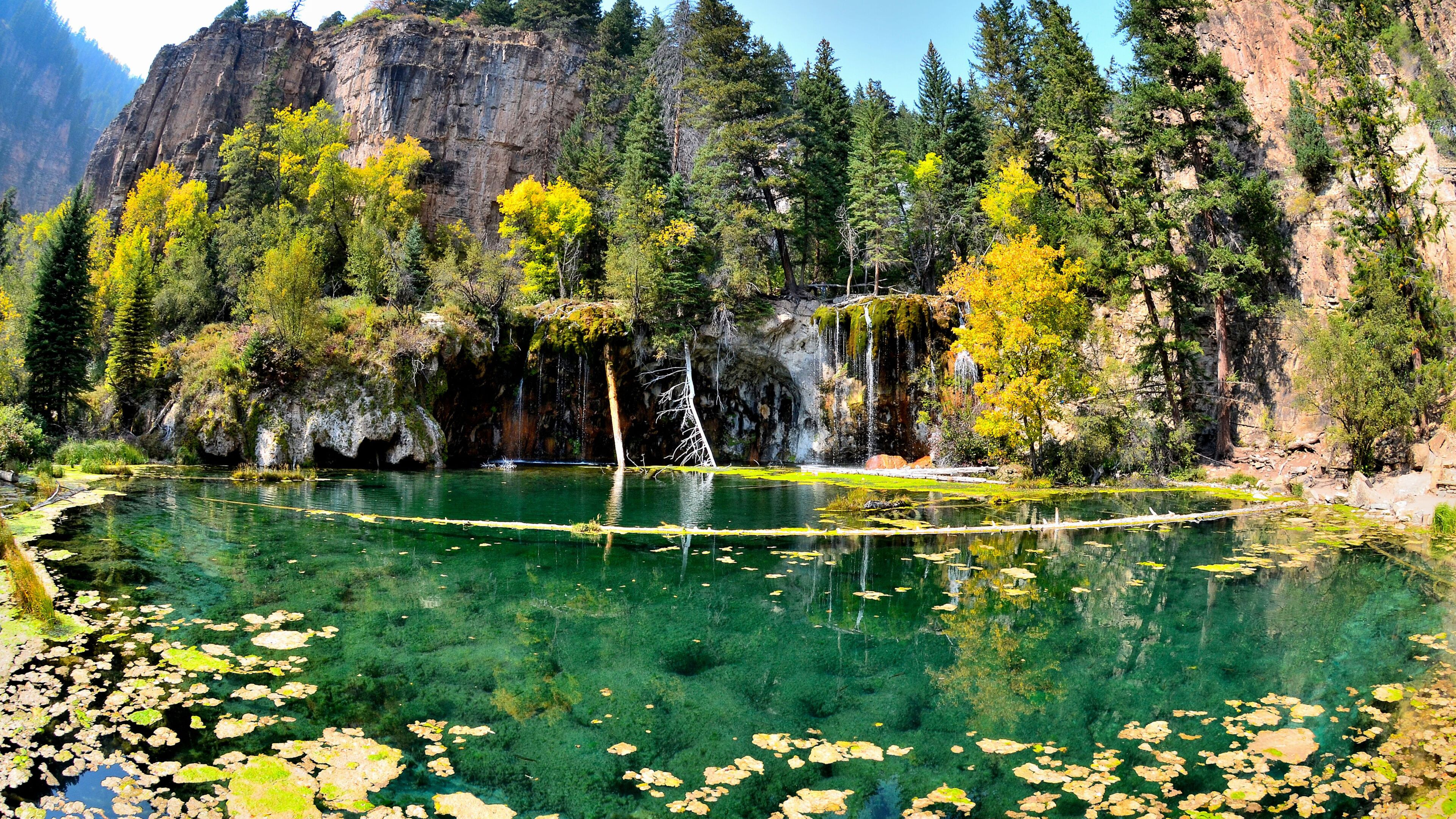 A clear mountain lake surrounded by dense forest and rocky cliffs.