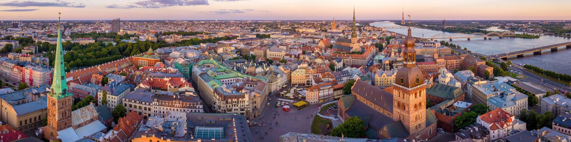 A panoramic view of a historic city with a prominent green spire, a river, and a bridge.