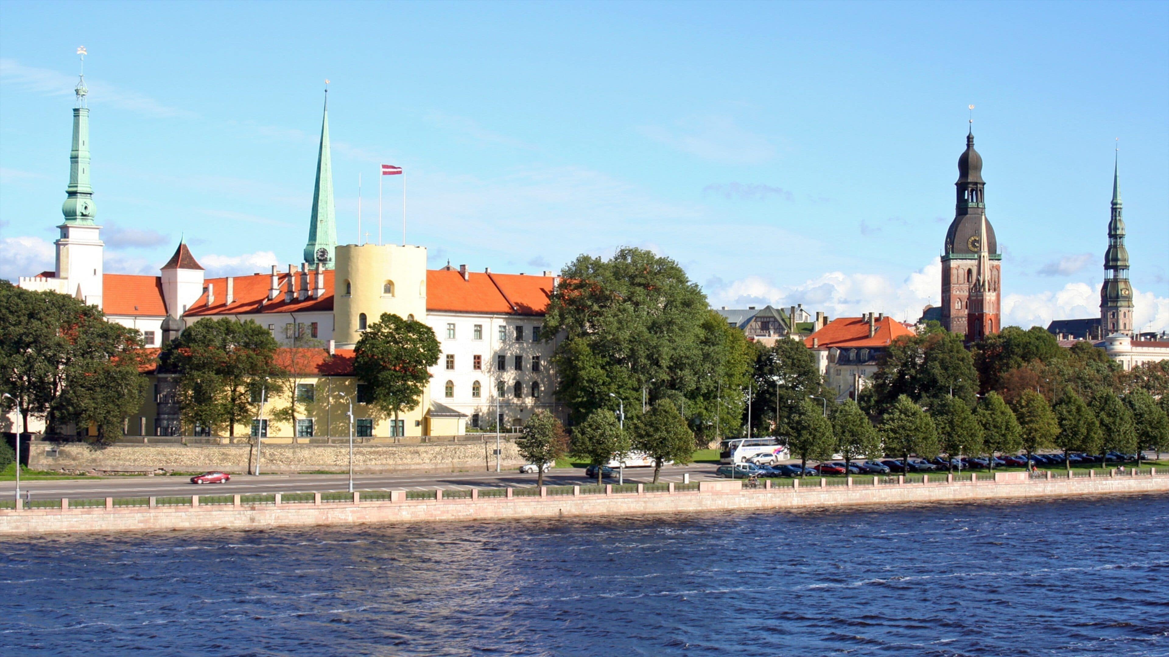 A riverside cityscape with historic buildings, a prominent church tower, and a castle-like structure.