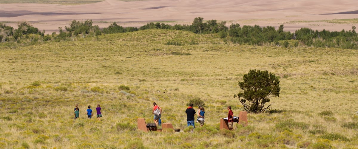 A group of people in a grassy field with sand dunes in the background.