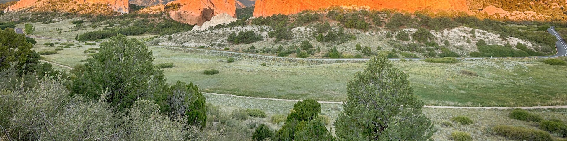 A mountainous landscape with prominent red rock formations and a winding road through a green valley.