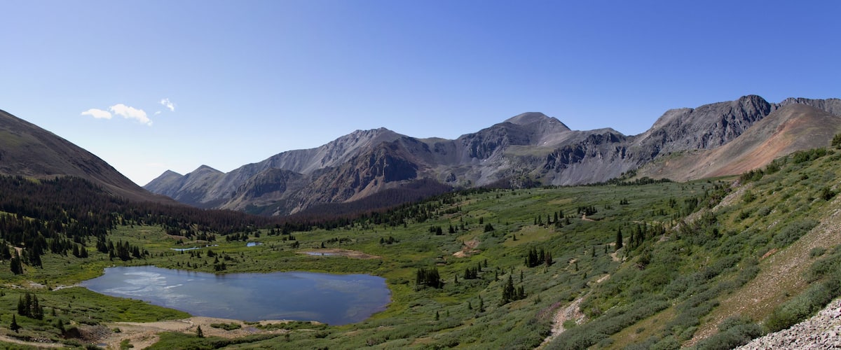 A mountainous landscape with a lake surrounded by green hills and rocky peaks.
