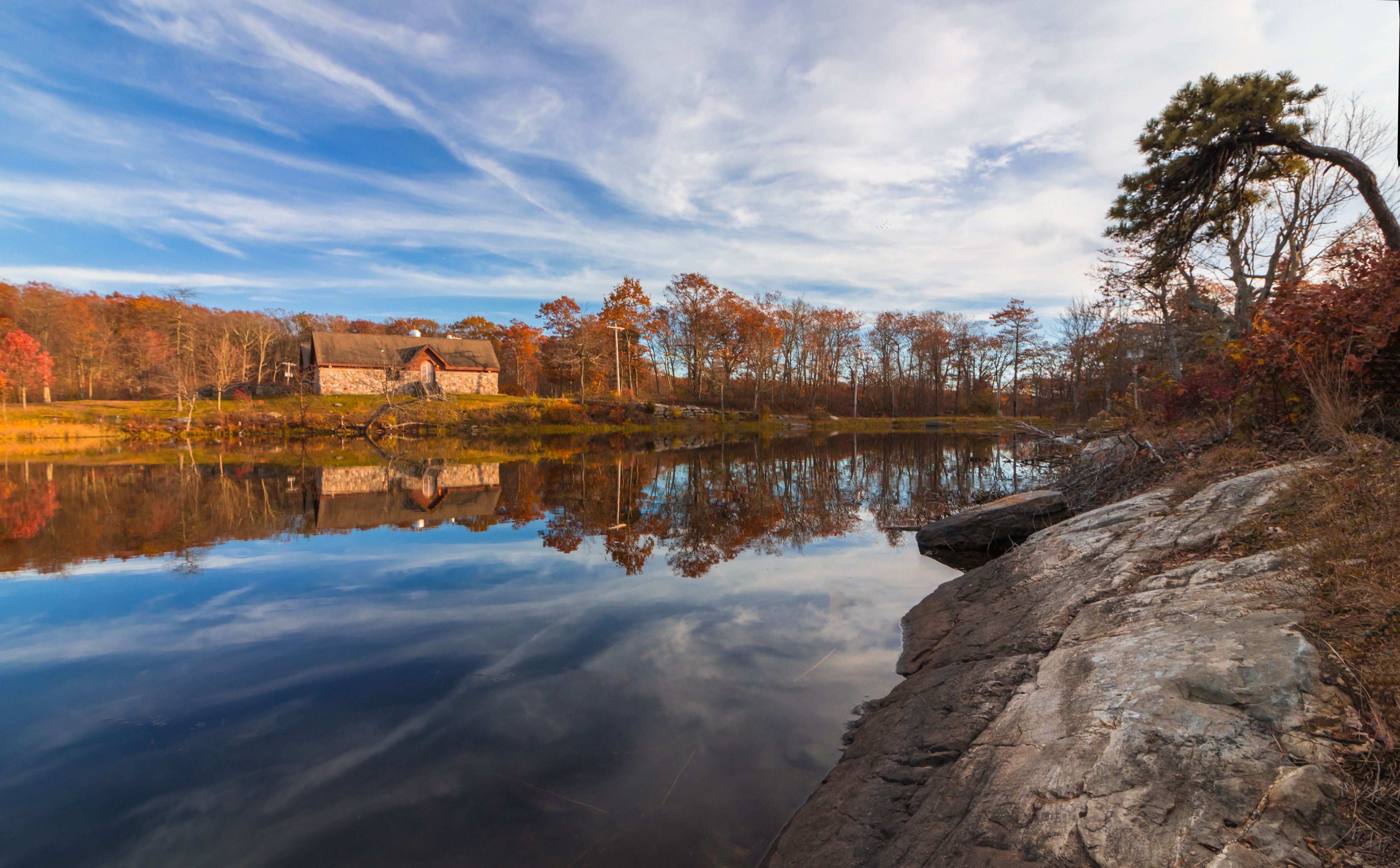 A calm lake reflecting a stone house and autumn trees.