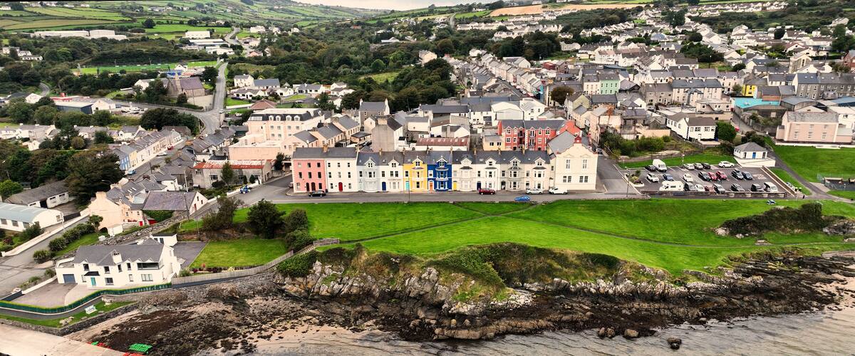 A coastal town with colorful buildings, a rocky shoreline, and a green field.