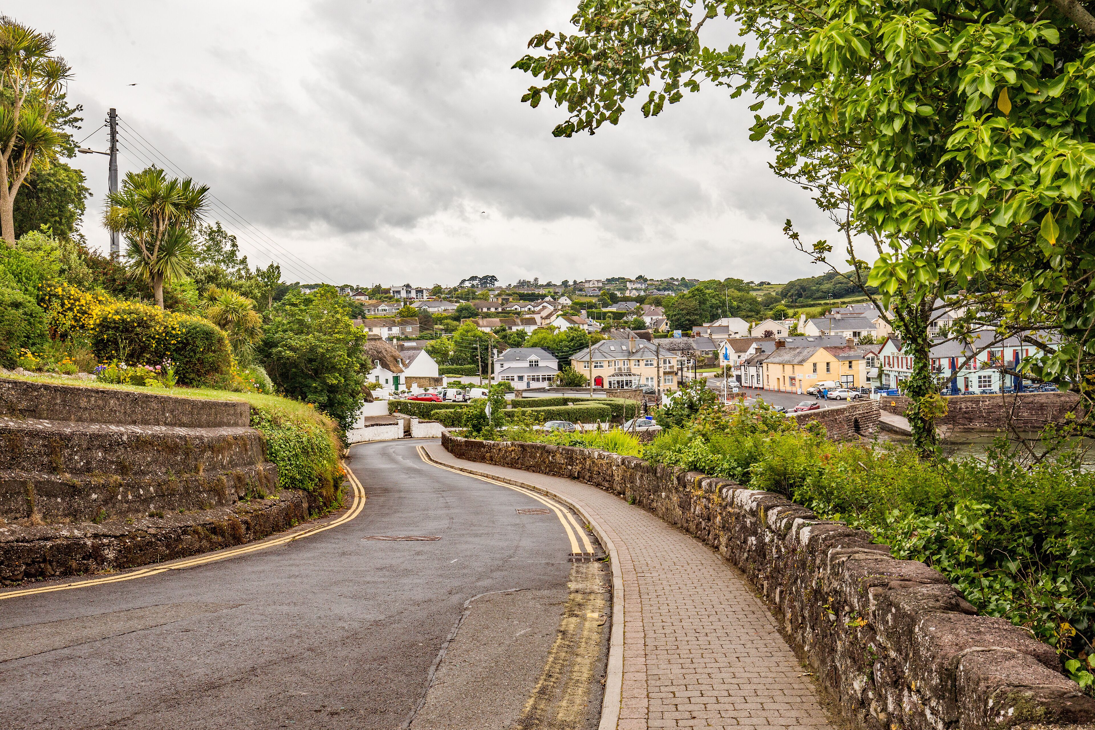 A curved road in a residential area with stone walls and greenery.