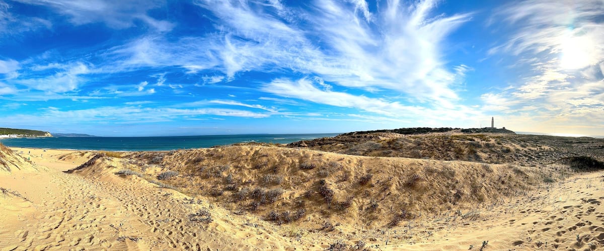 A coastal landscape with sand dunes, a lighthouse, and the ocean.