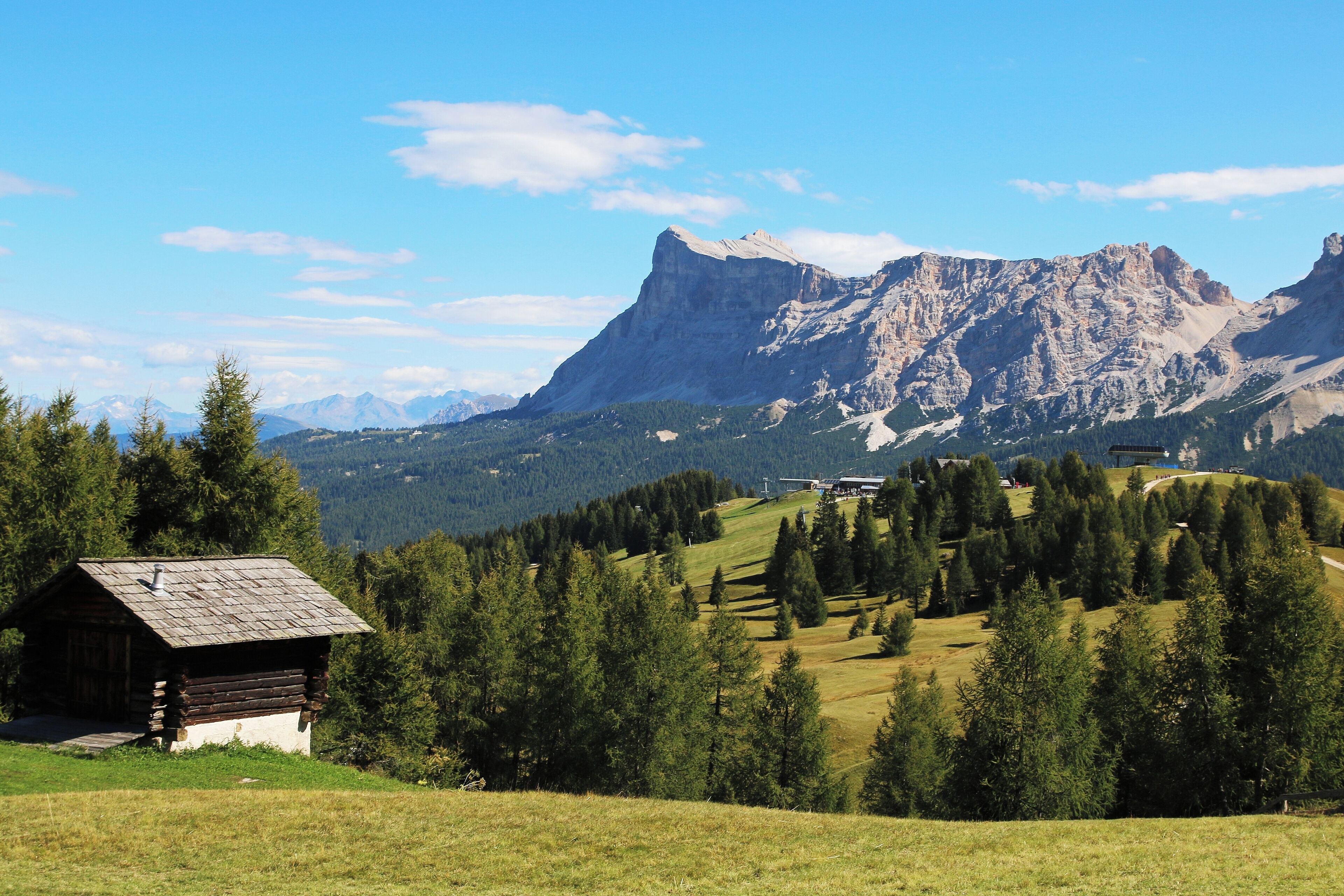 A wooden cabin in a grassy field with a mountain range in the background.