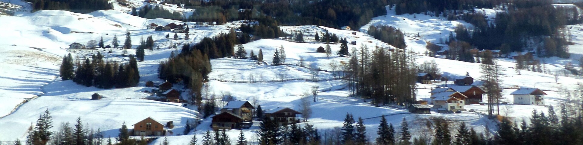 Un pueblo cubierto de nieve en la montaña, con casas y bosques densos.