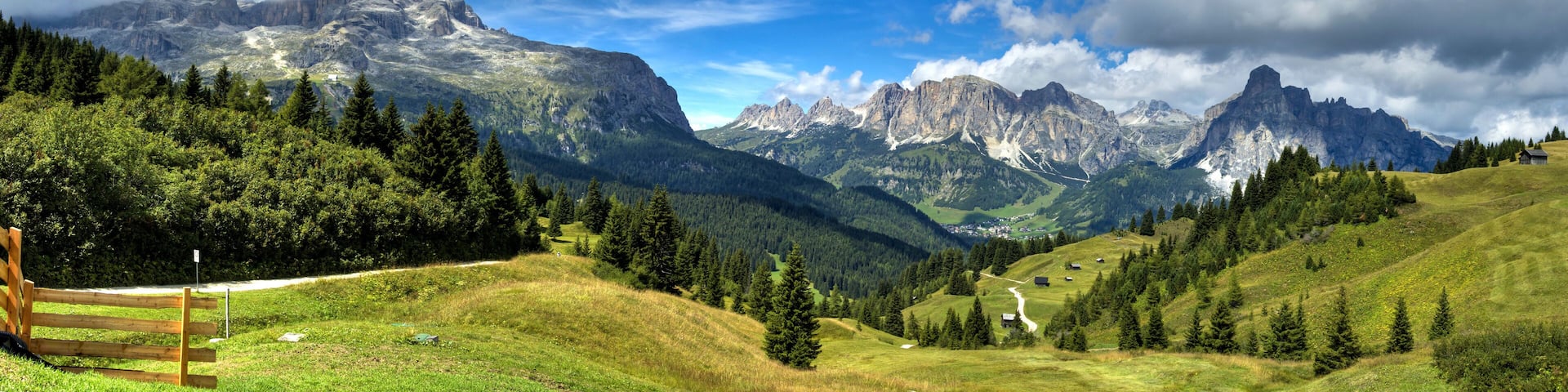 A mountainous landscape with a wooden bench, dense forest, and a village in the valley.