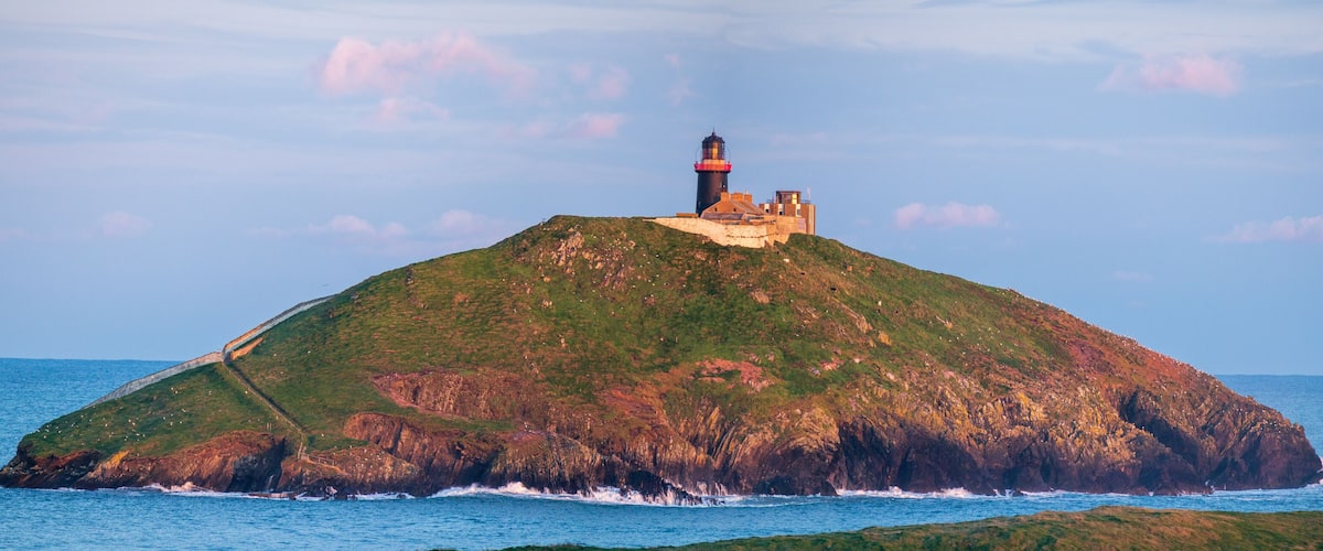 A lighthouse on a rocky island with the ocean in the background.