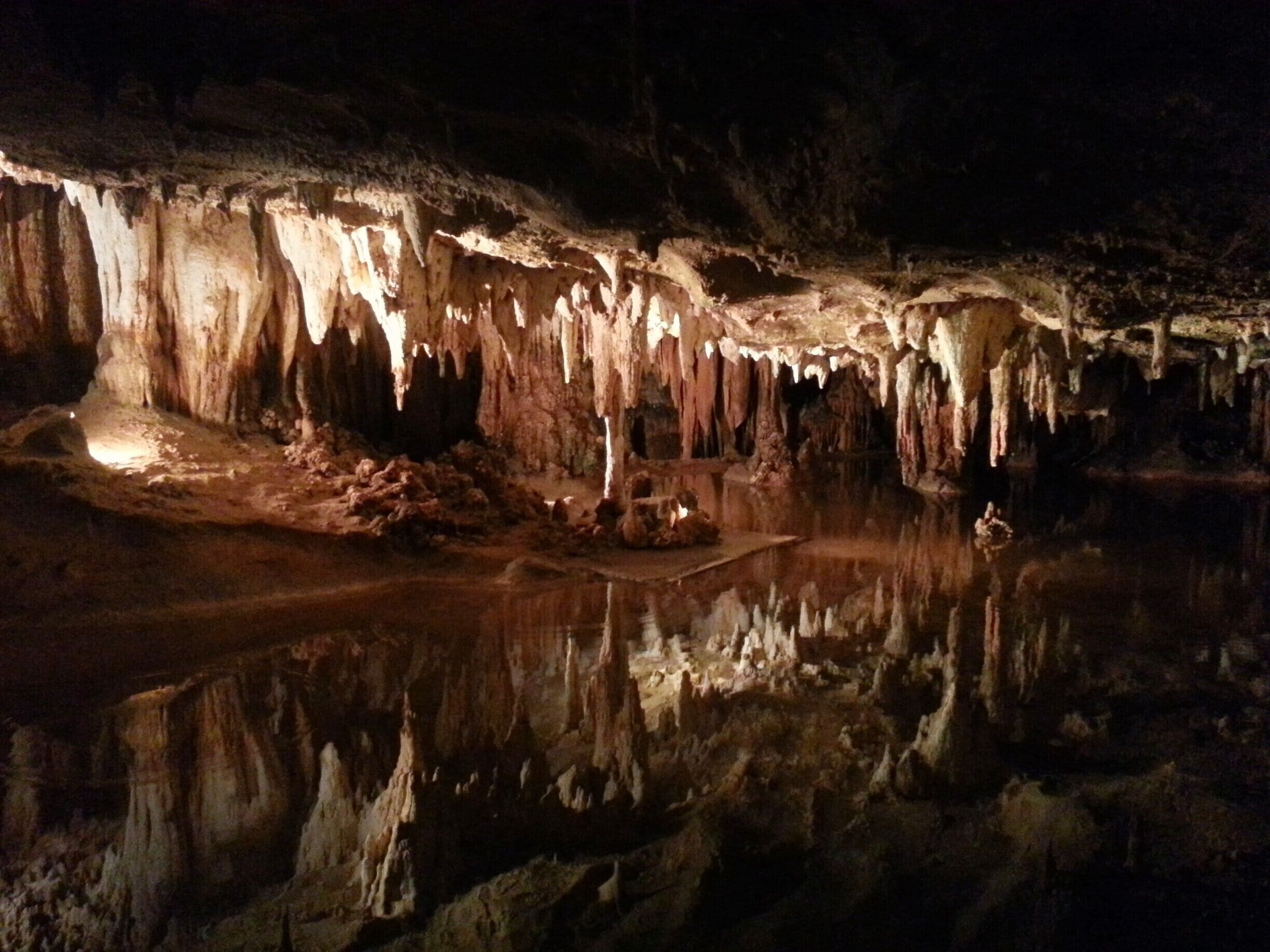 A cave with stalactites and stalagmites, a reflective pool, and a small cave opening.