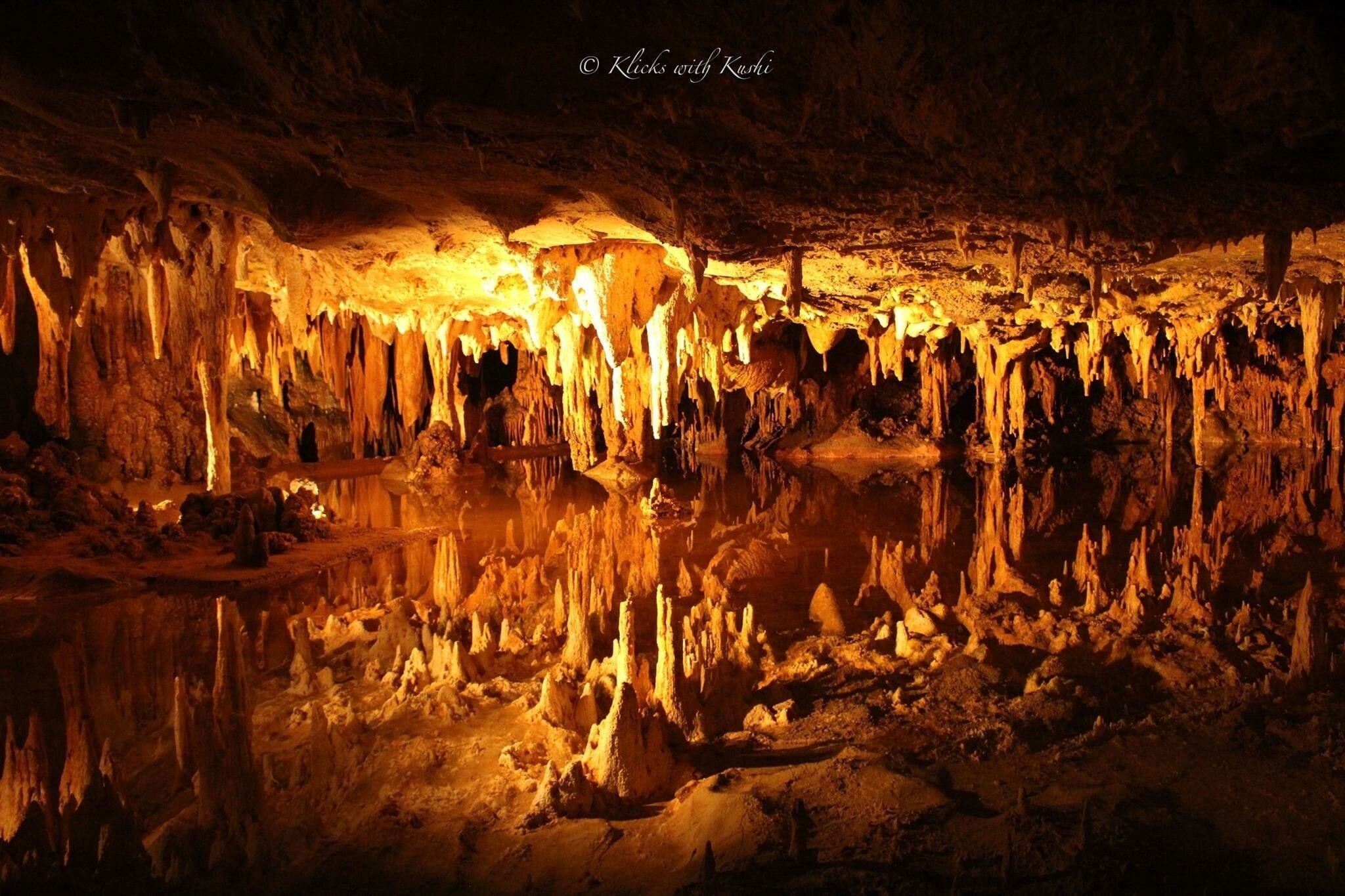 A cave with stalactites and stalagmites illuminated by artificial lighting.