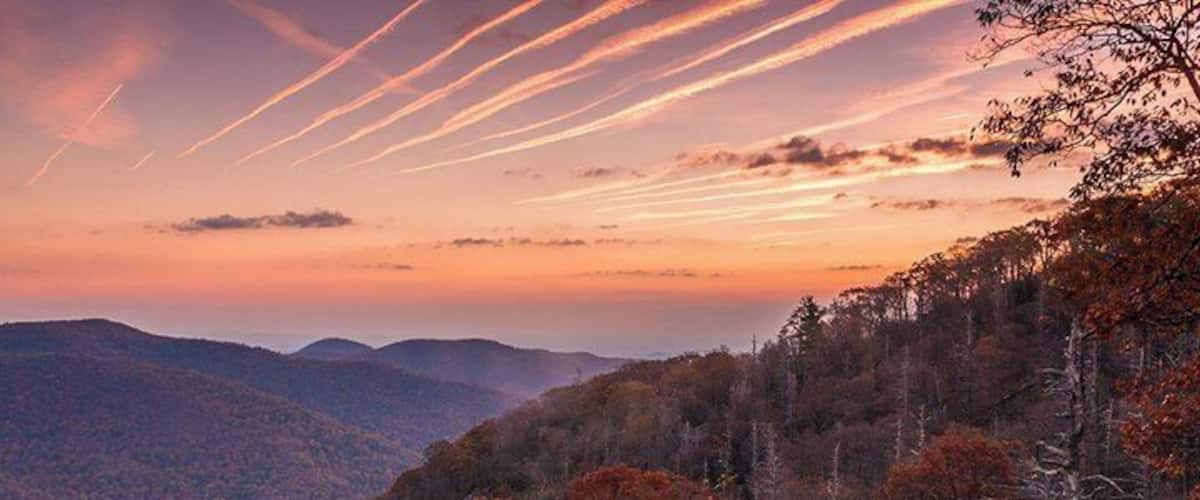 Une chaîne de montagnes boisée au coucher du soleil, avec des traînées de nuages dans le ciel.