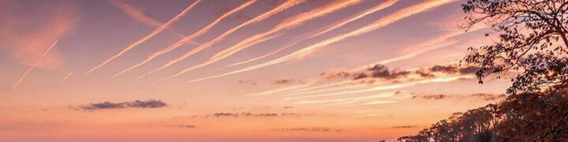 A forested mountain range at sunset with streaks of clouds in the sky.