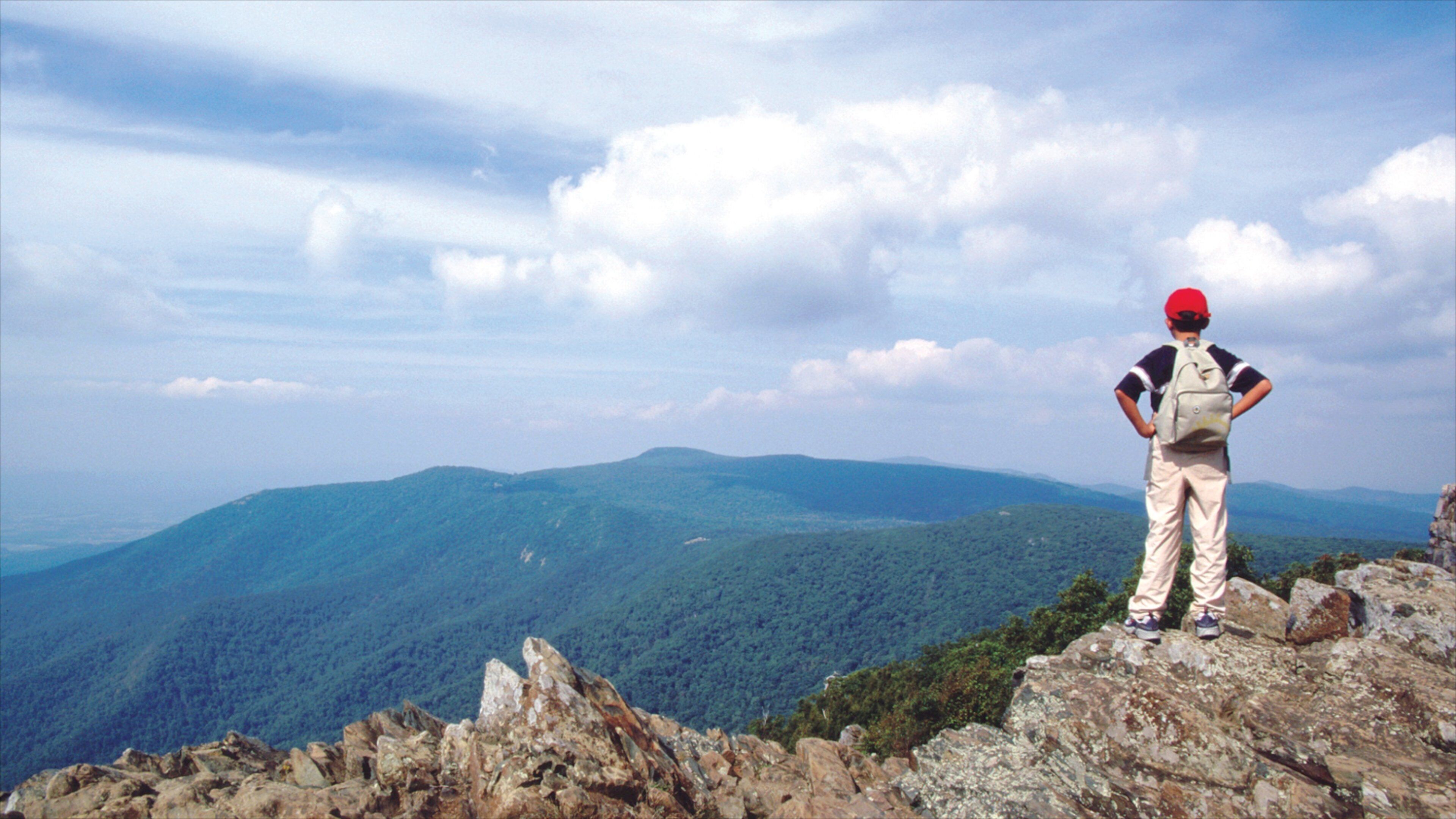 A hiker on a rocky outcrop overlooking a mountainous landscape.