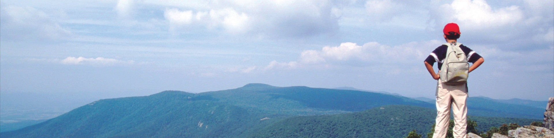 A hiker on a rocky outcrop overlooking a mountainous landscape.