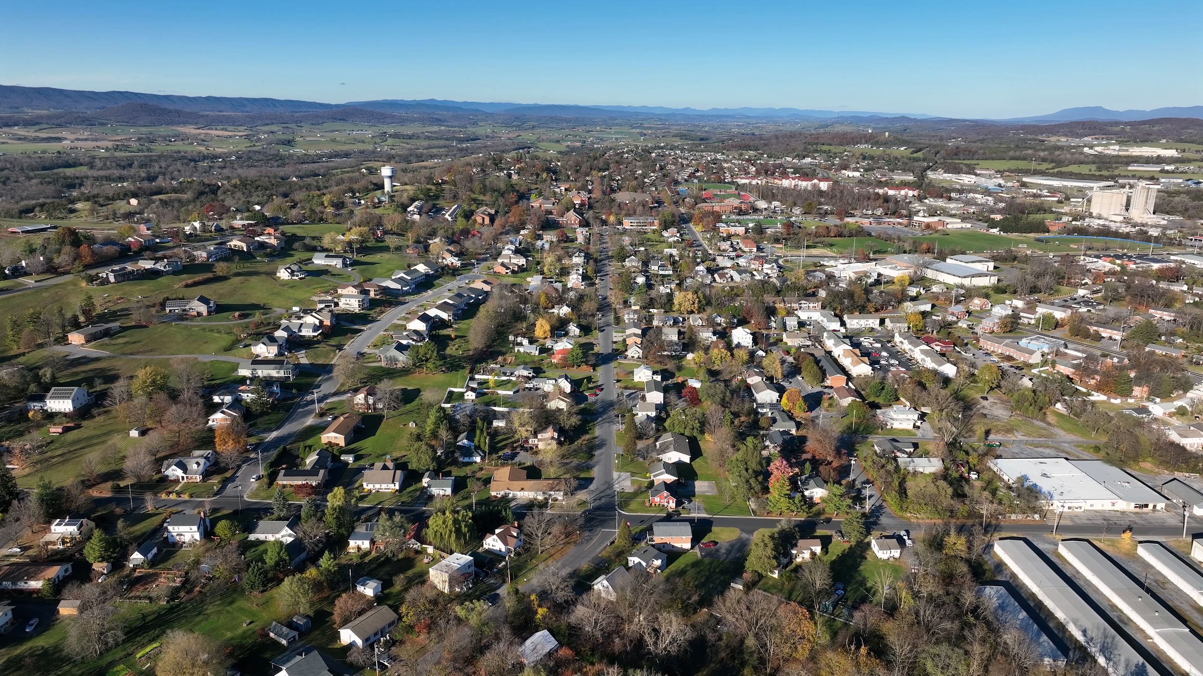 Aerial view of the city of Harrisonburg with residential neighborhoods, local roads, and autumn foliage under a clear blue sky in Harrisonburg, Virginia, United States.